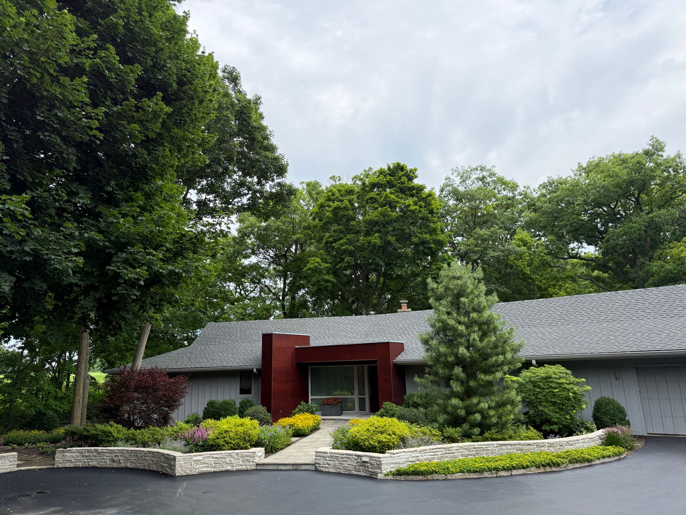 A modern home framed by curved limestone walls, pine, and layered plantings